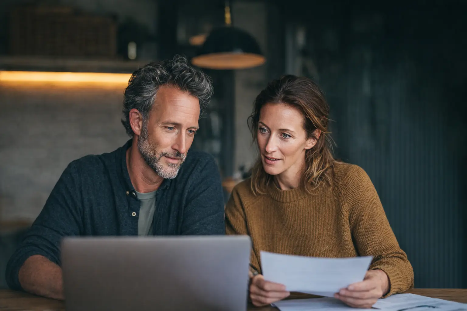 A couple in their early 40s reviewing investment statements at a home office desk with a laptop showing portfolio performance, representing a review of tax-loss harvesting opportunities in a taxable brokerage account.
